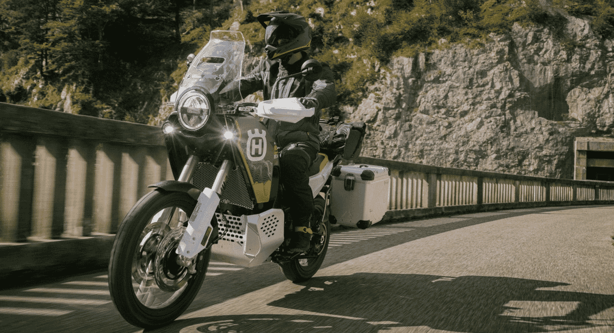 A motorcyclist in all-black protective gear riding a Husqvarna on a winding mountain road.