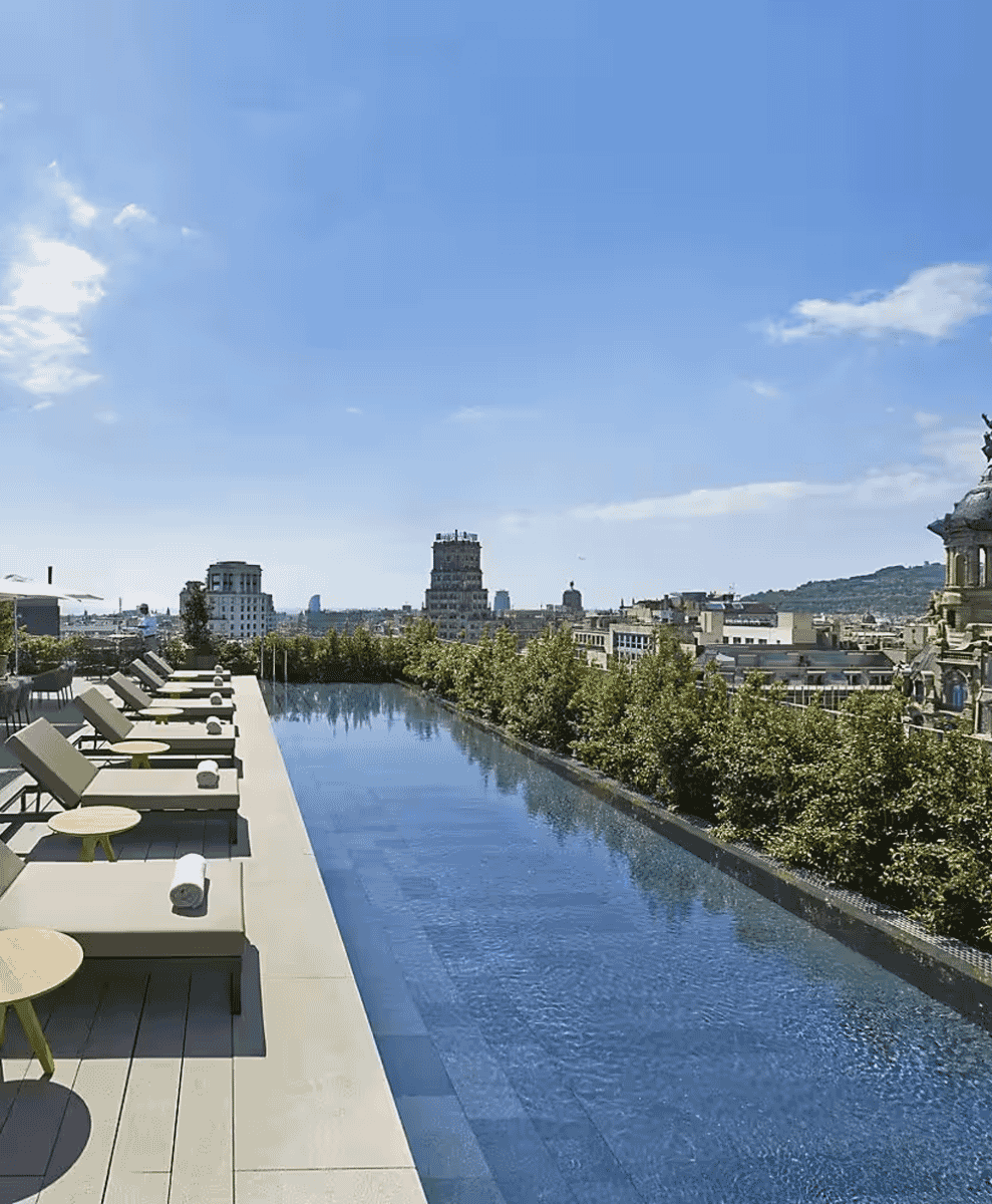 A luxury rooftop infinity pool overlooking a modern European cityscape under a clear blue sky.