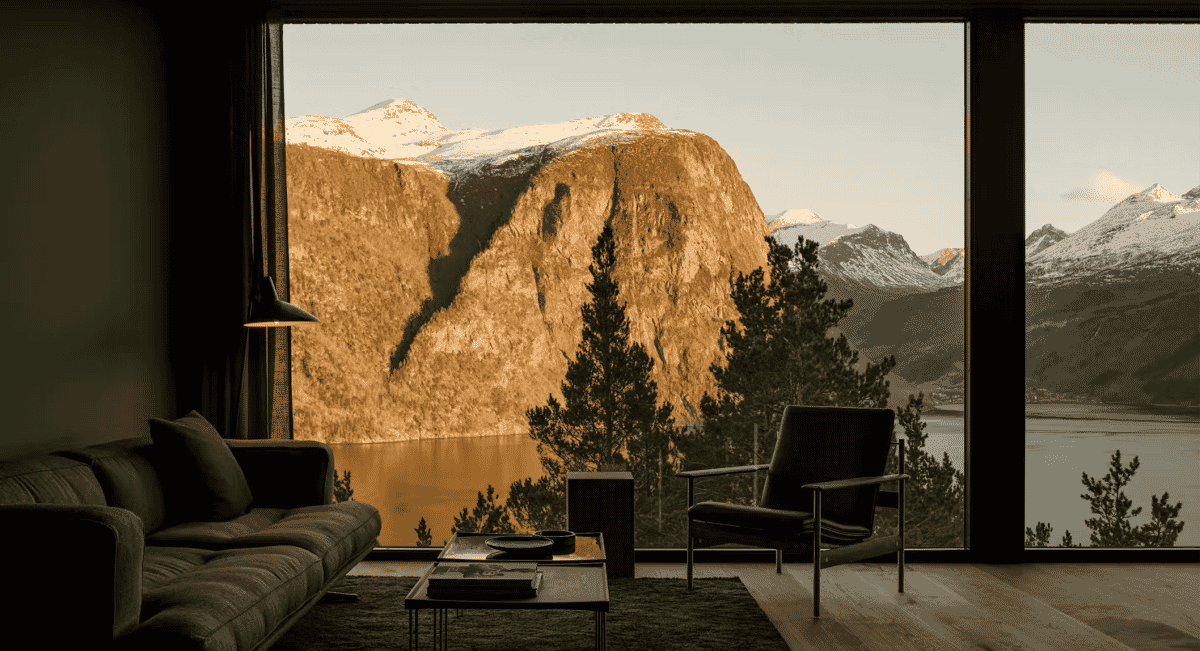 Modern minimalist living room with sleek furniture overlooking snow-capped mountains and a fjord.