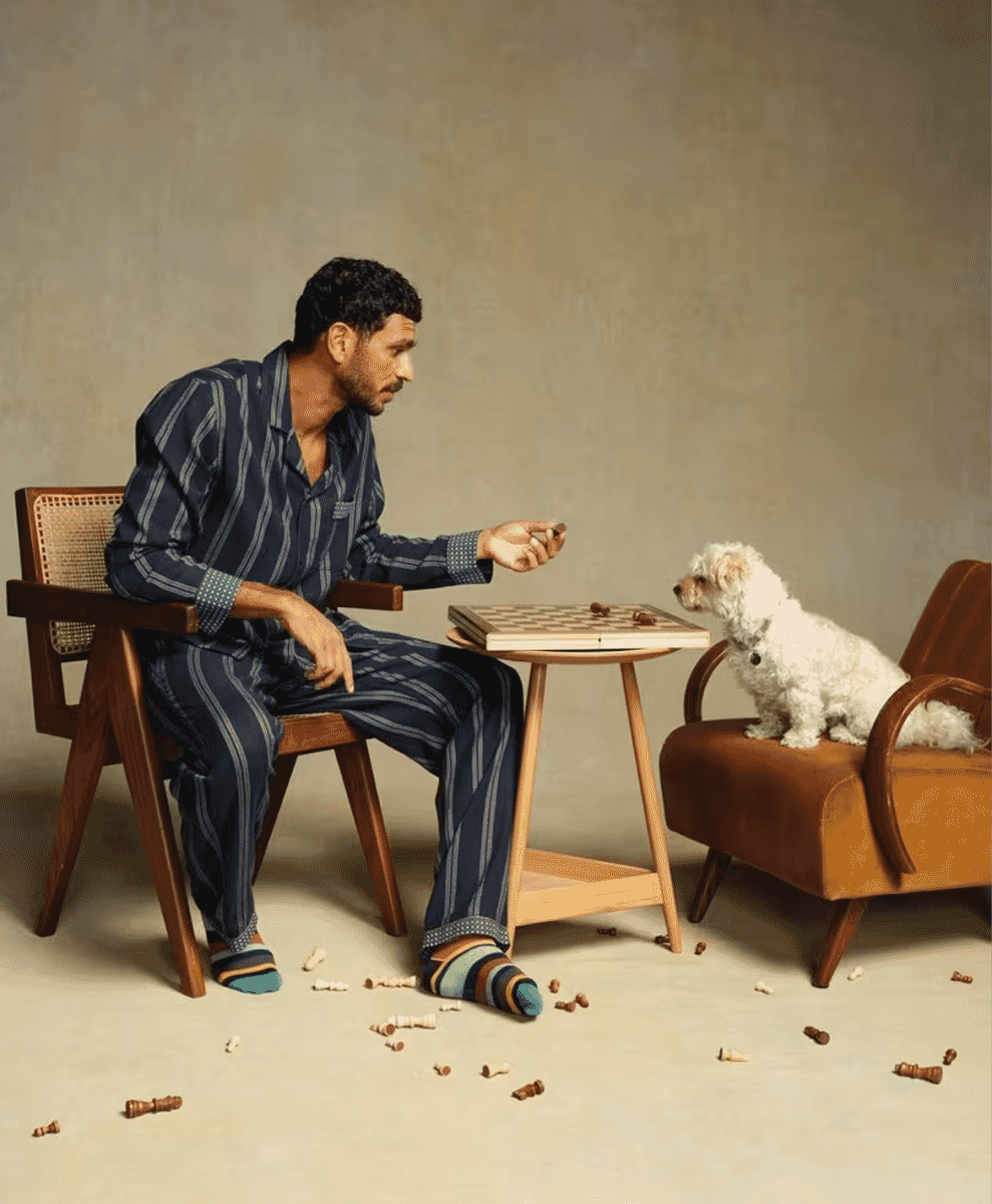 A man in navy blue vertical striped pajamas playing chess with a white dog.