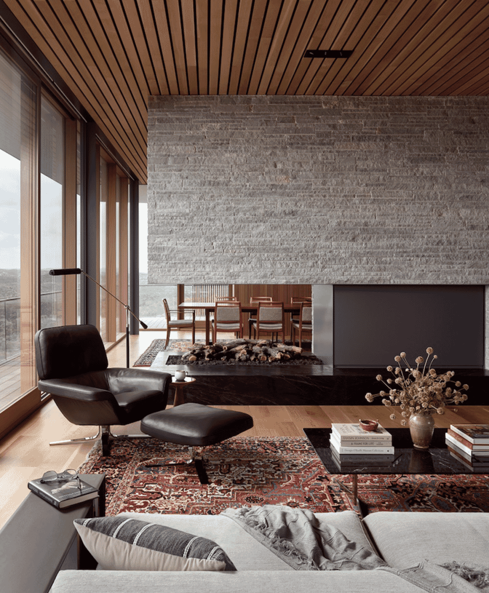Modern living room featuring a stone fireplace and large windows overlooking a scenic landscape.