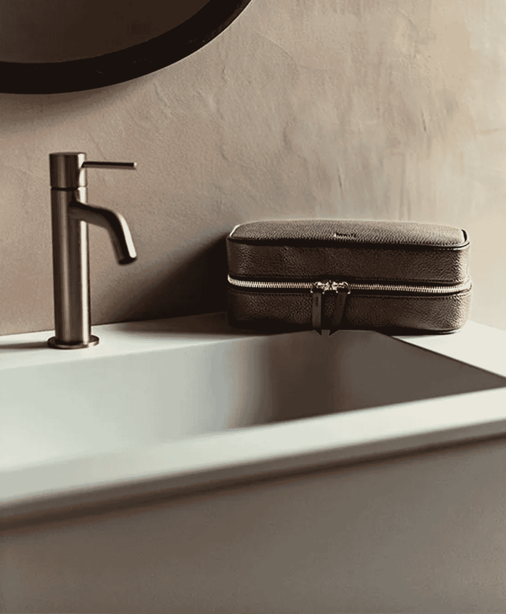 Brown textured leather wash bag sitting on a modern bathroom sink beside a black faucet.