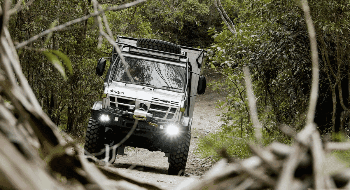 A white Arksen U1700 navigating a narrow dirt trail through a lush green forest.