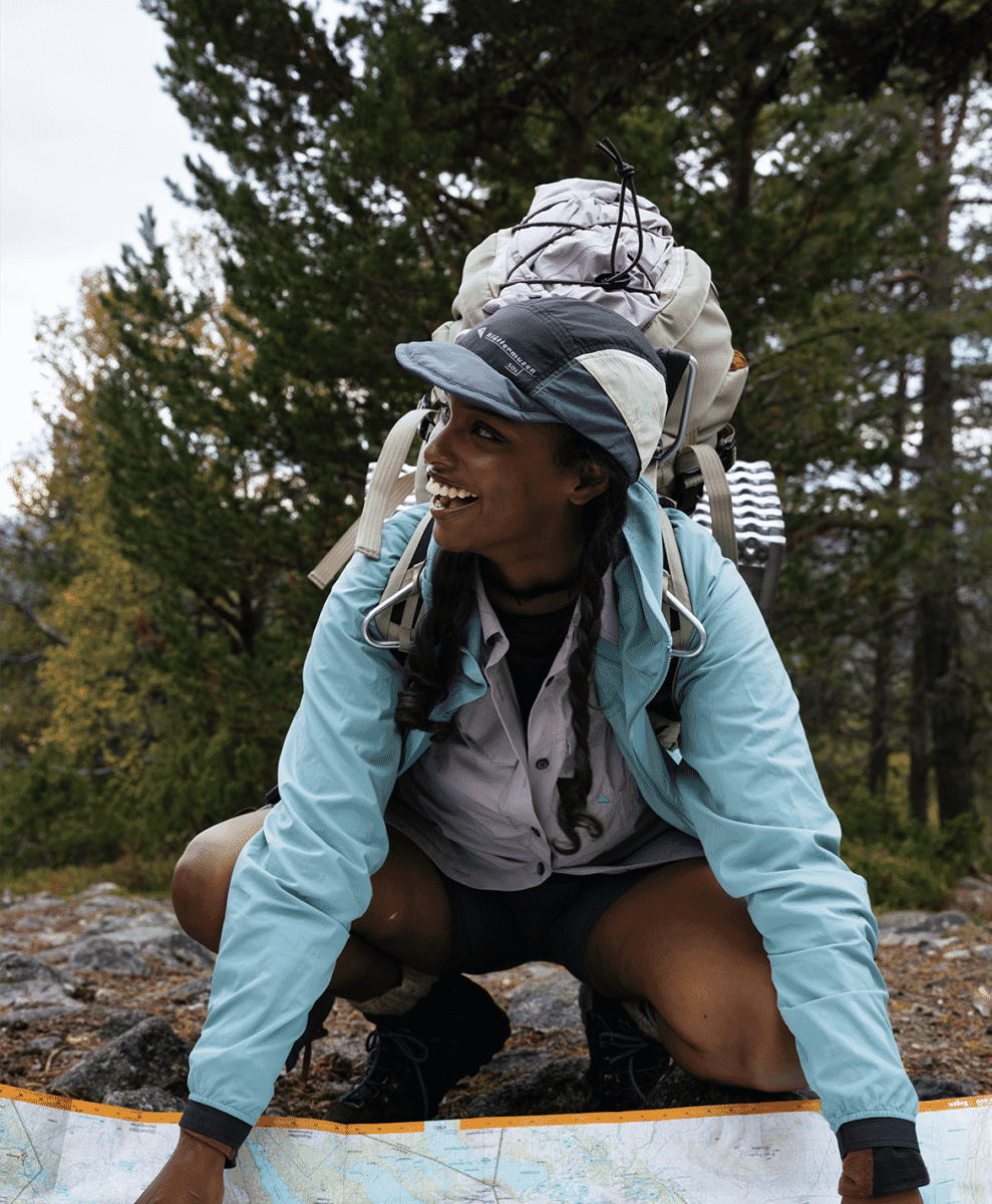 A hiker with a backpack and light blue jacket reviewing a map in a forest.