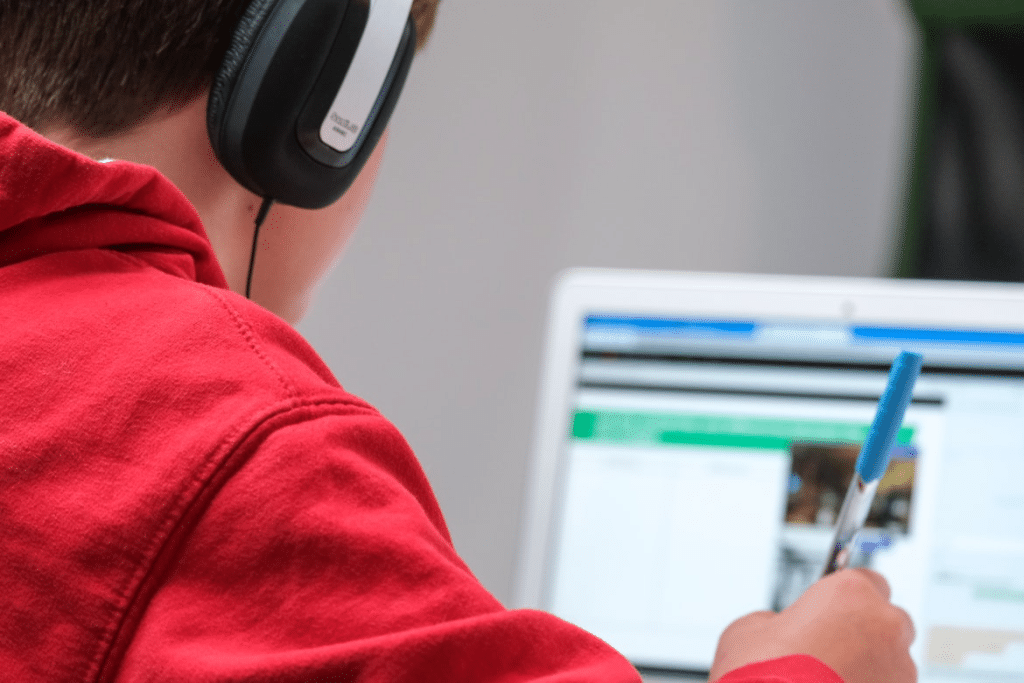A person in a red hooded sweatshirt wearing black over-ear headphones works on a laptop.