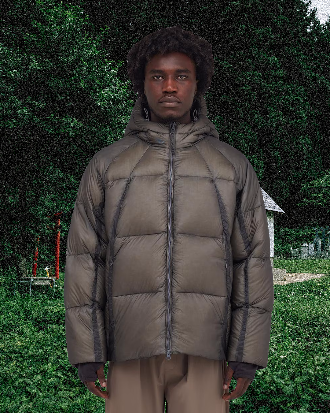 Man in a taupe puffer jacket in a lush green outdoor setting.