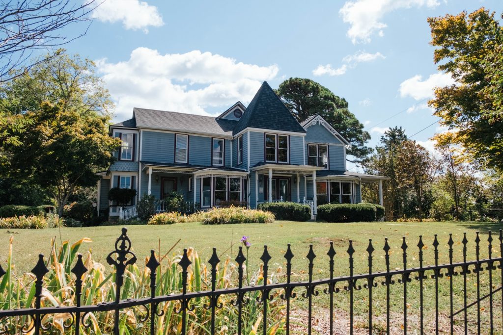 Victorian blue house with an ornate black fence and thick, healthy green grass.