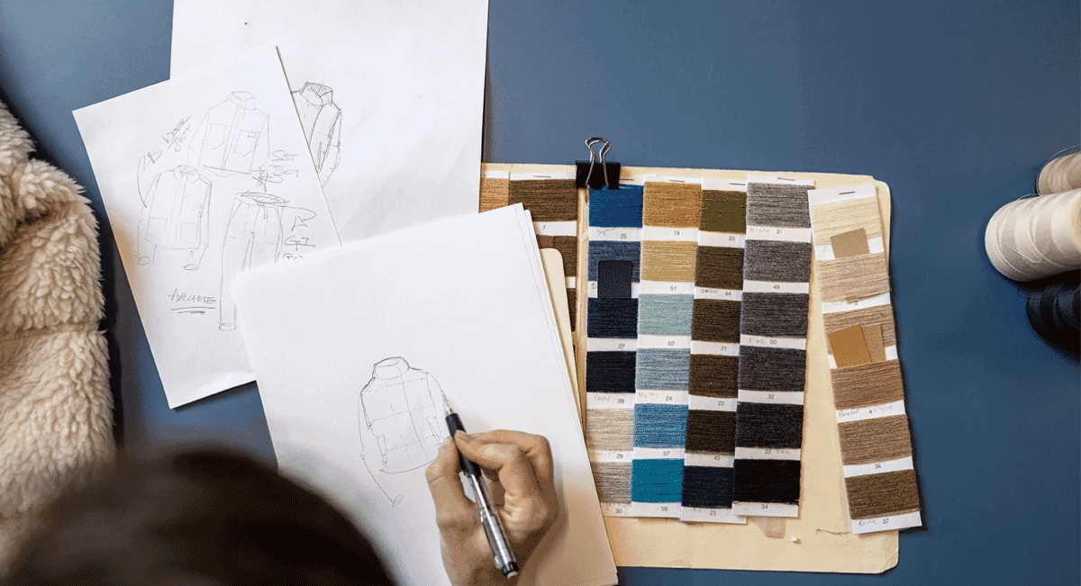 A designer sketching an apparel prototype at a desk with fabric swatches.