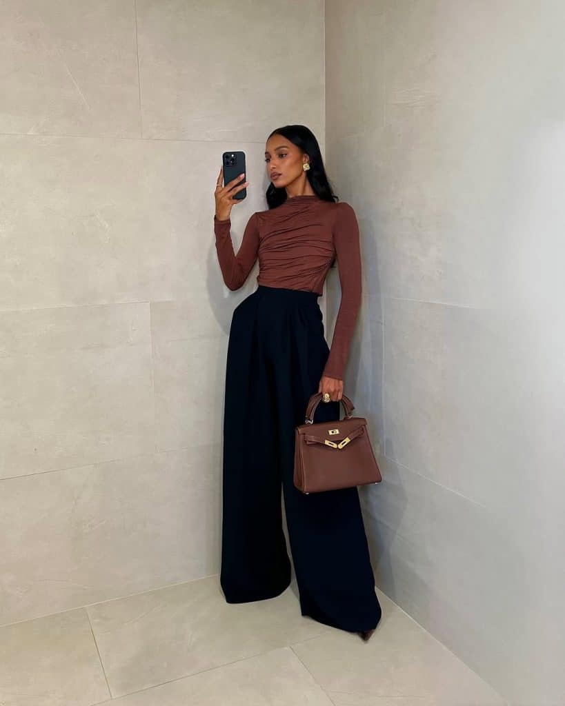 Mirror selfie of a woman wearing a ruched brown long-sleeve top and black wide-leg trousers.