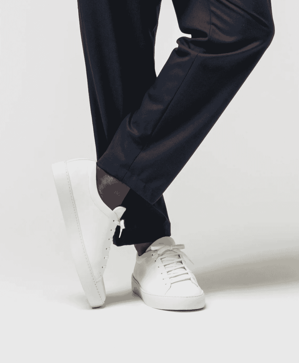 Close-up of sleek white leather sneakers with dark tailored trousers