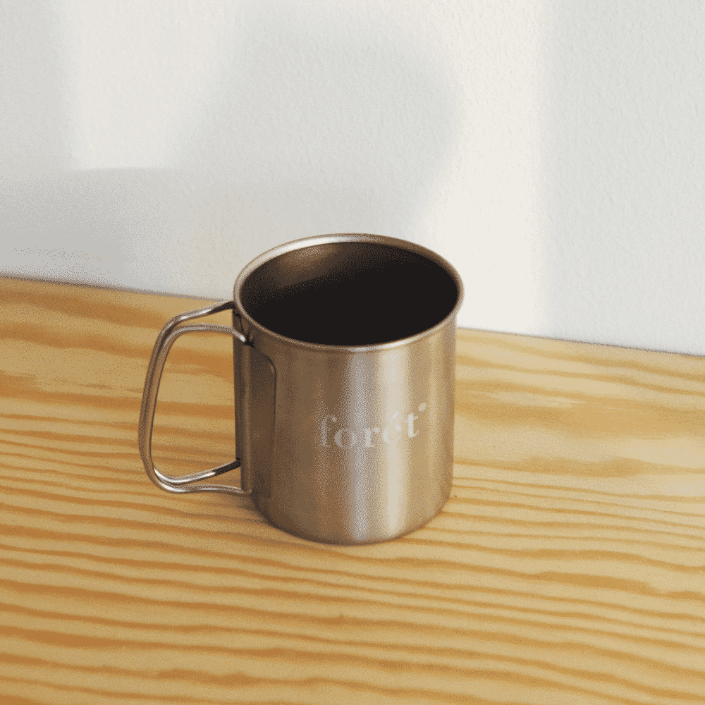 Close-up of a stainless steel camping mug with 'forêt' branding on a wooden surface.