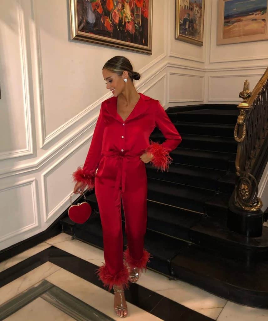 Woman in a vibrant red satin jumpsuit with feathered cuffs walking down a staircase.