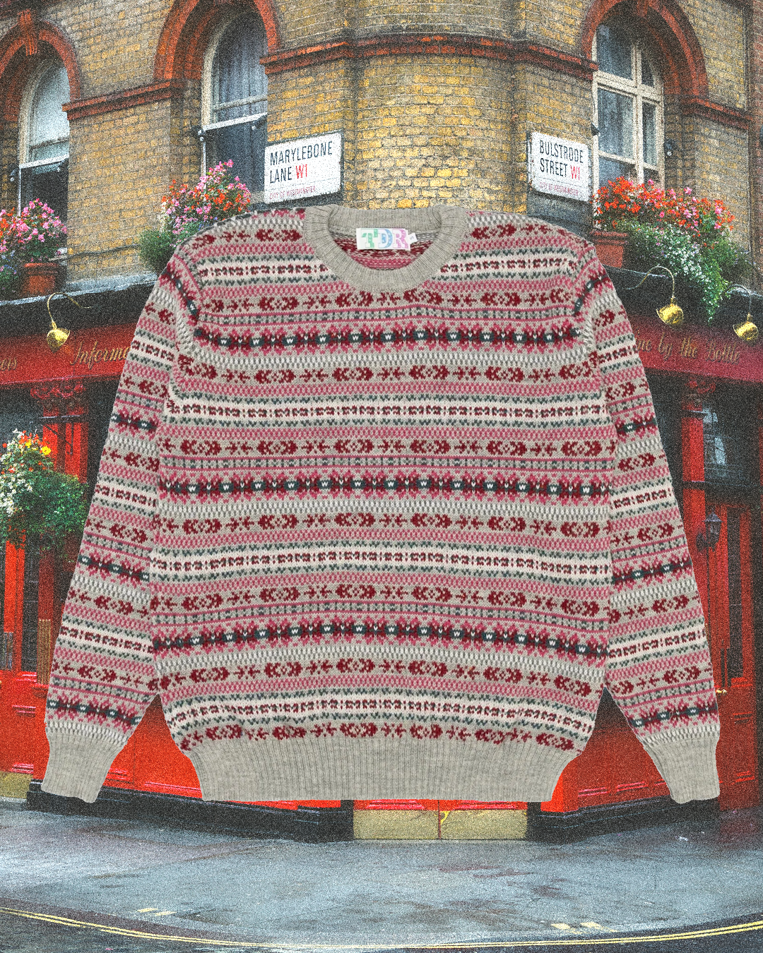 A vintage-style Fair Isle sweater with red, grey, and white patterns in front of a classic London pub corner.