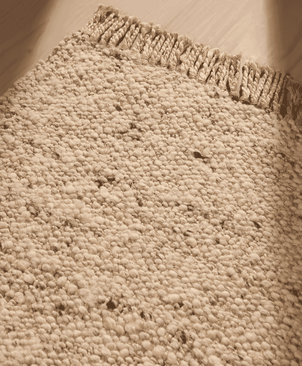 Close-up of a textured beige woven rug with fringed edges.