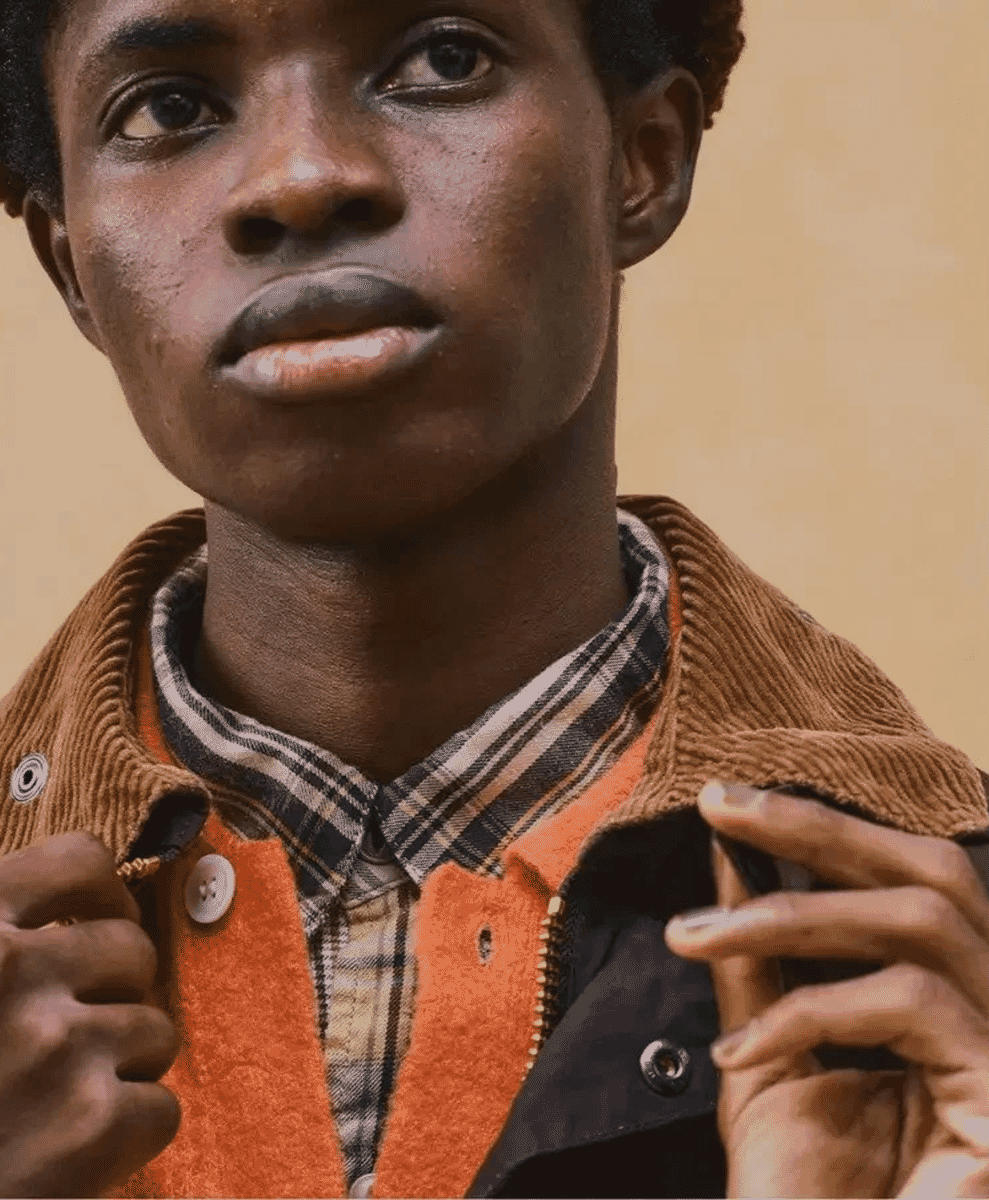 Close-up of layered menswear featuring an orange fleece vest and plaid shirt under a brown jacket.