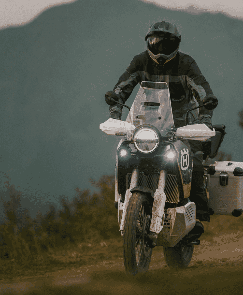 A rider in rugged touring gear navigating a technical dirt trail on a motorcycle.
