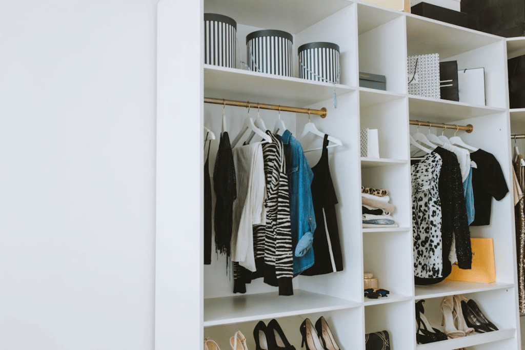 Neatly organized white closet shelves with striped tops, denim jackets, and decorative storage boxes.