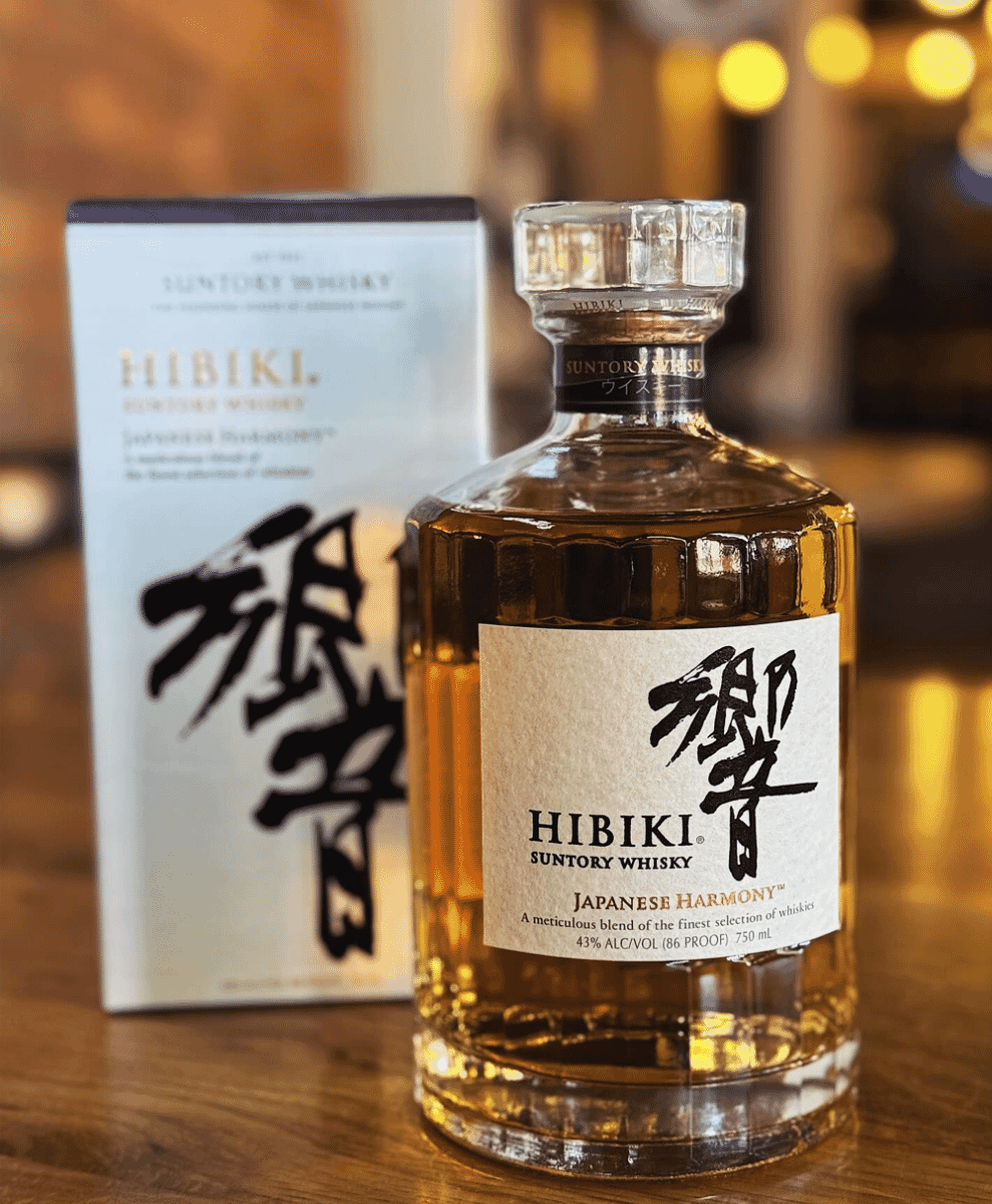 Bottle of Hibiki Suntory Whisky on a wooden surface with a warm bokeh background.