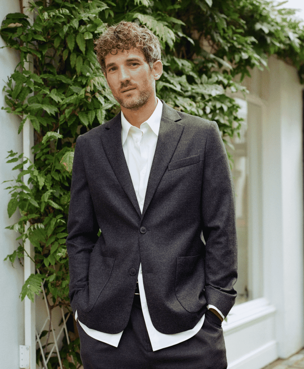 A man wearing a dark gray wool blazer over a white shirt in an outdoor setting.
