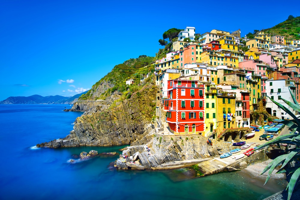 Close-up of vibrant multi-colored houses clinging to a rocky cliffside above turquoise water.