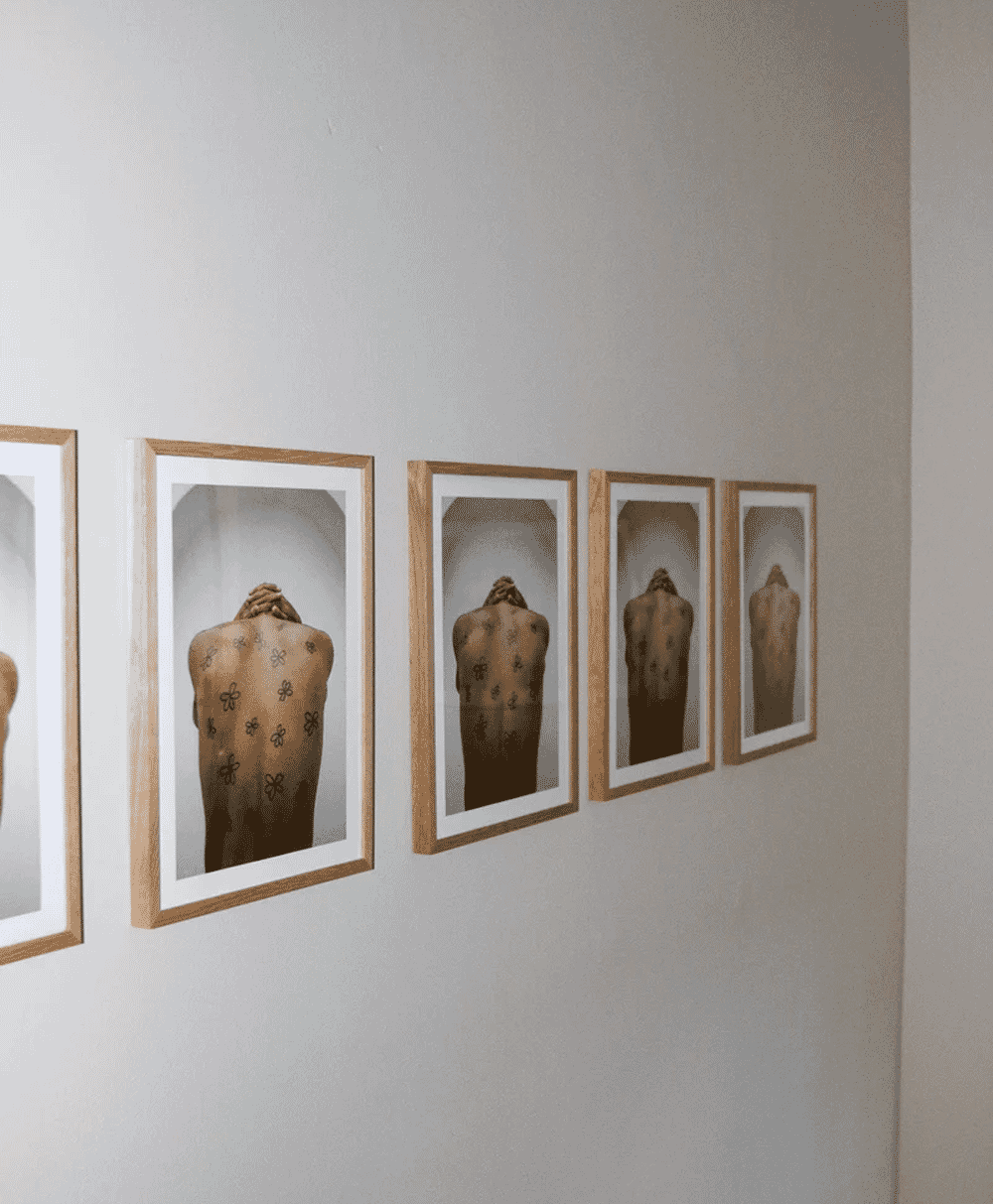 Three framed photographs showing a person's back with intricate floral tattoos, arranged in a horizontal row on a wall.