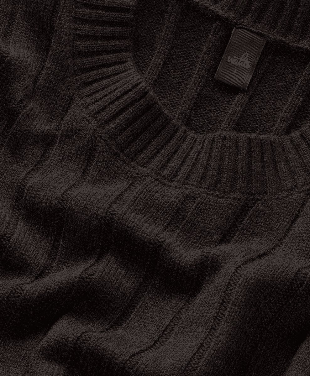Close-up of the textured cable patterns on a black ribbed knit sweater.