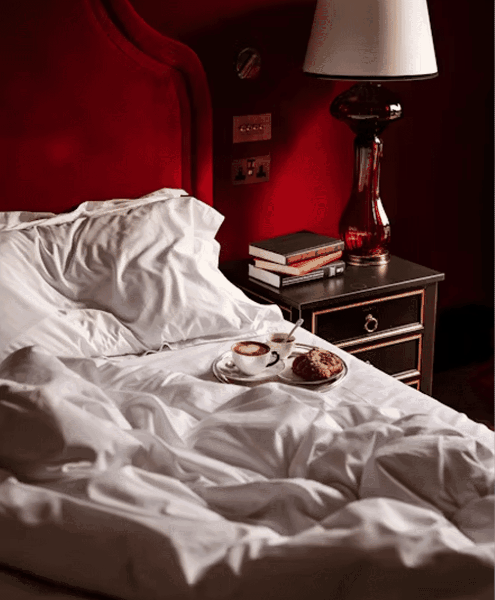 Cozy bedroom detail with a red velvet headboard and white rumpled linens.