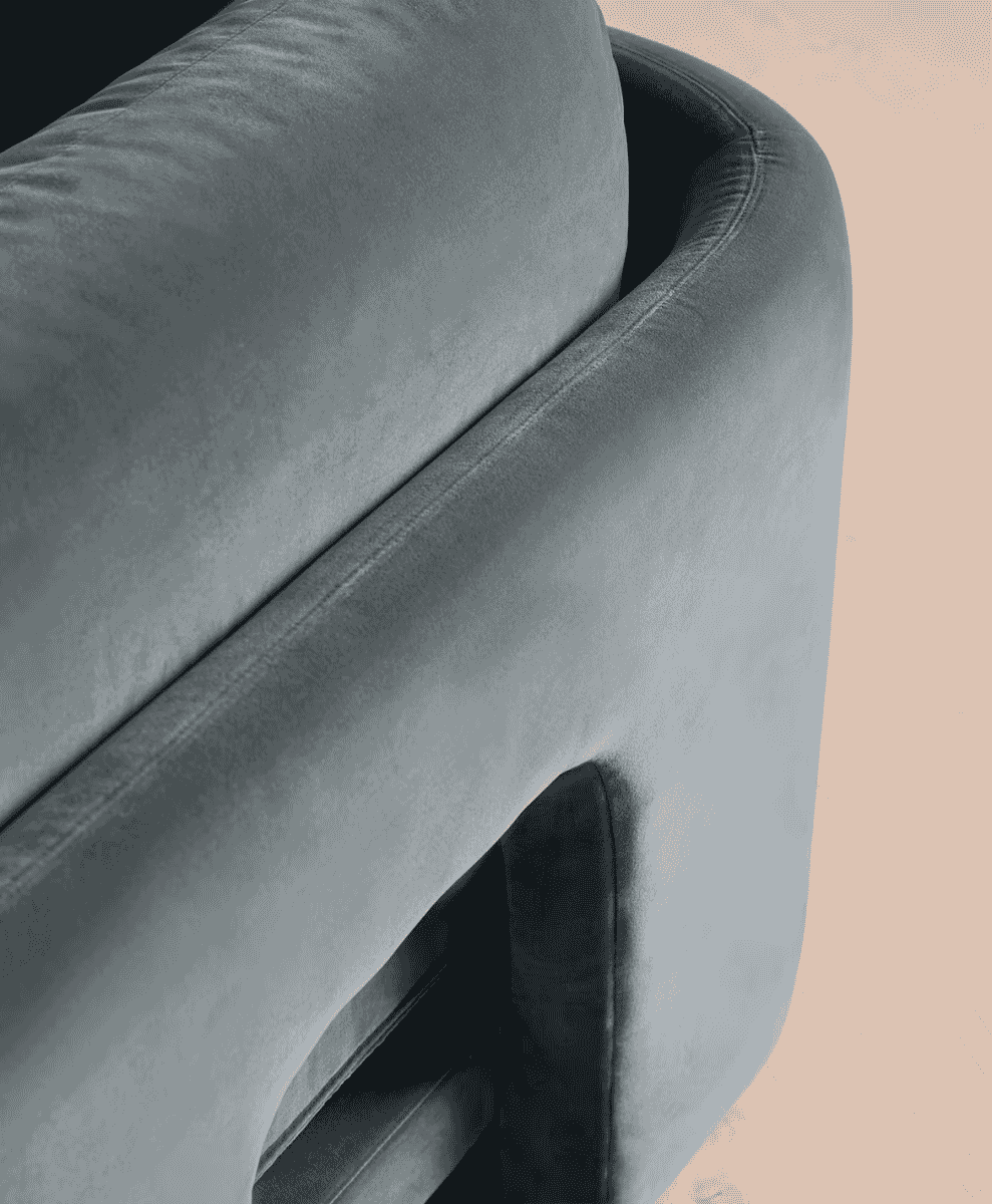 Gray velvet modular sofa with curved armrests against a soft peach background.