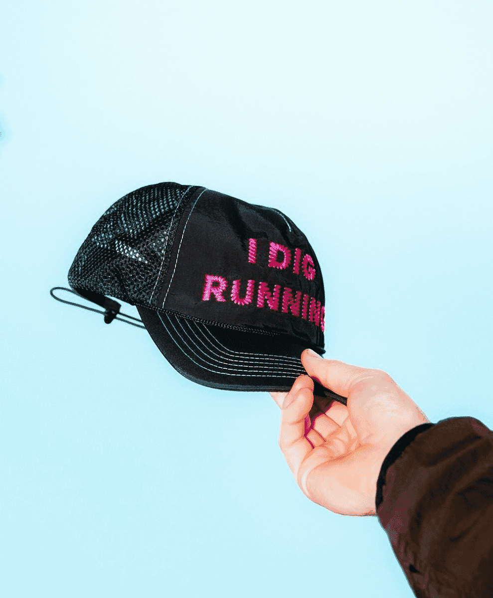 A close-up of a black mesh trucker hat with pink embroidery reading 'I DIG RUNNING'.