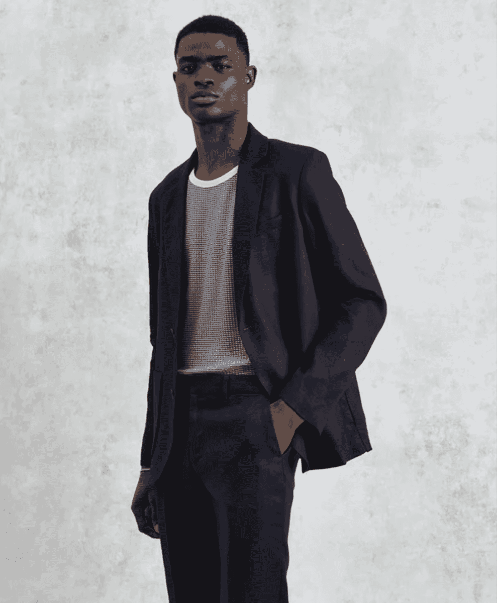 A man modeling a dark textured blazer over a ribbed knit sweater against a studio background.