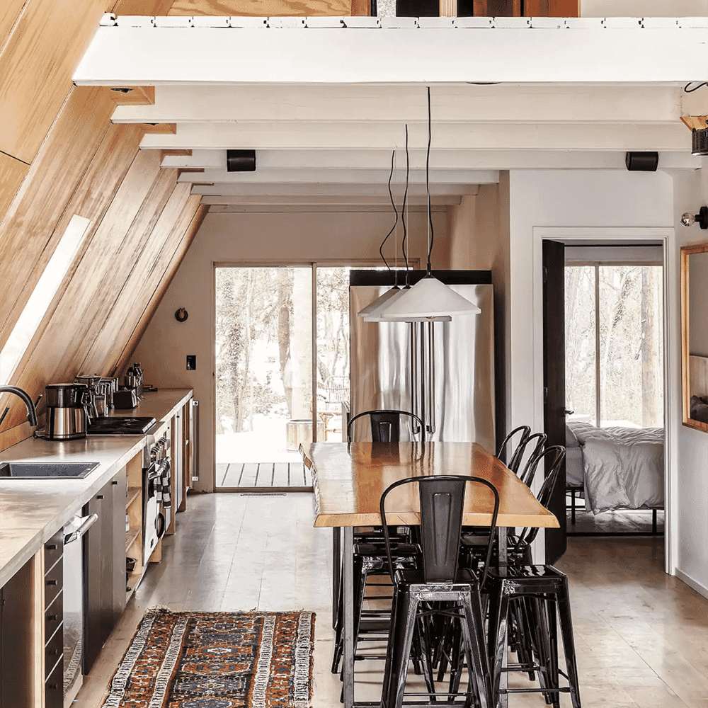 Modern rustic kitchen and dining area with wooden beams overlooking snowy trees.
