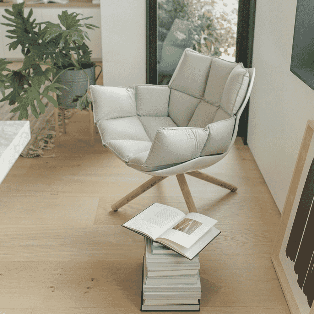 A white cushioned armchair in a bright room with books and green plants.