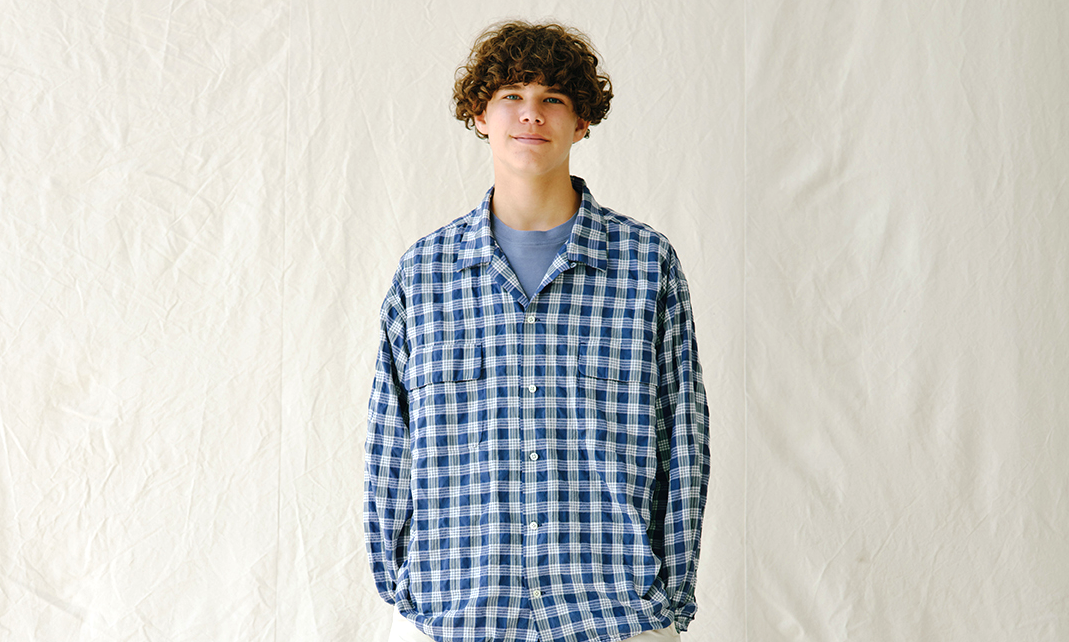 Young man in a layered blue and white plaid button-up shirt over a gray tee.