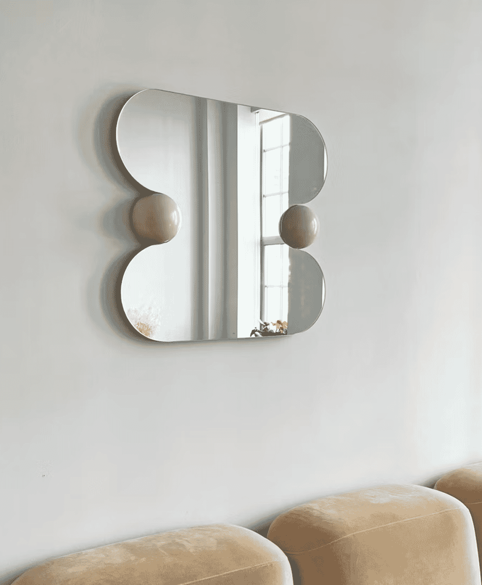Cloud-shaped frameless mirror reflecting a minimalist living room with beige seating.