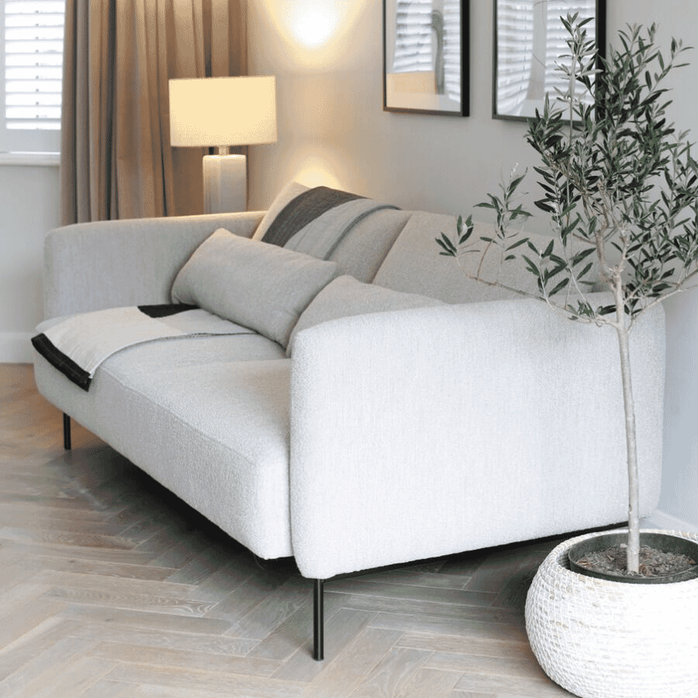 A white textured sofa accompanied by a tall olive tree in a pot and warm, glowing ambient lighting.