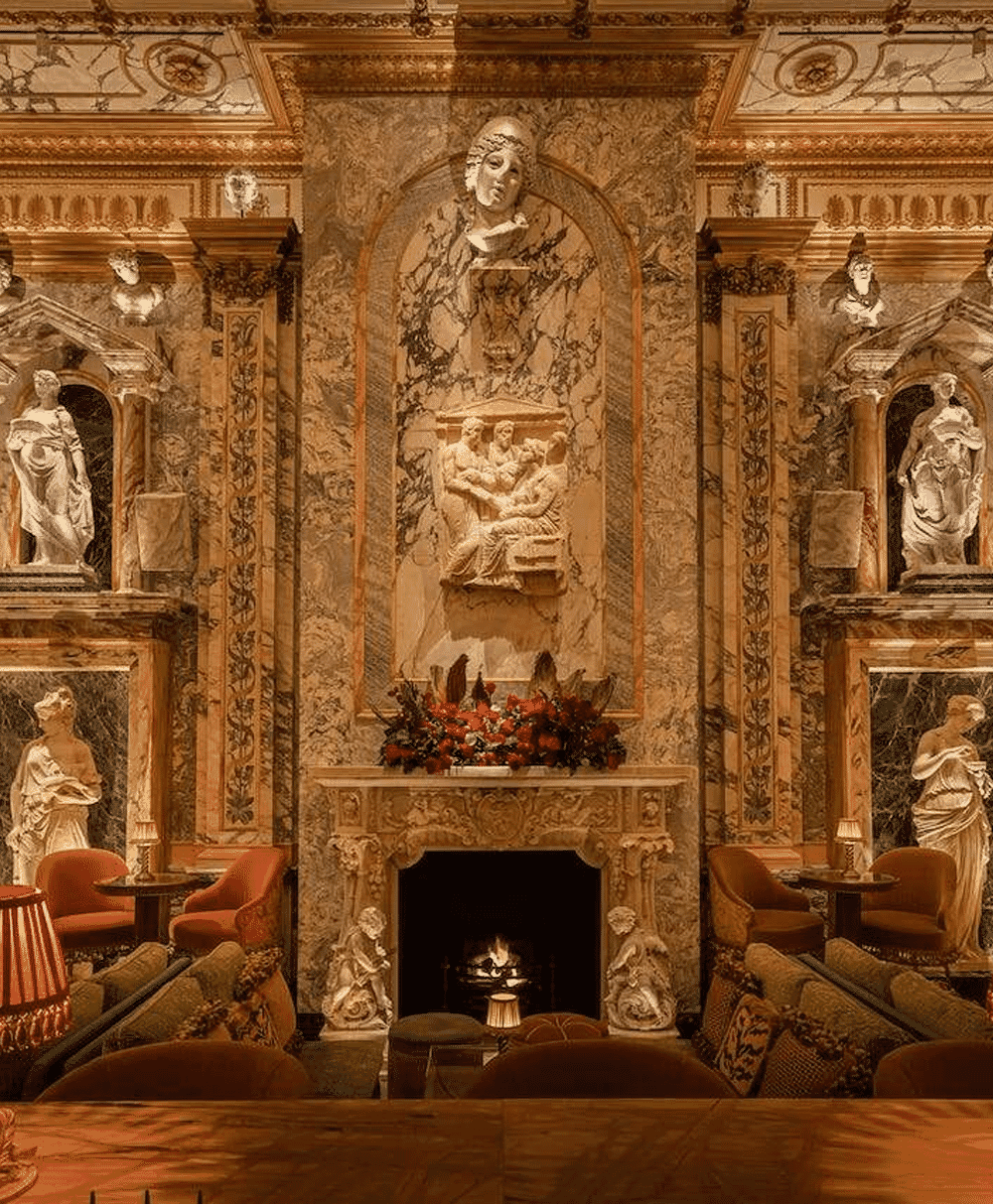 Opulent marble-clad interior with classical sculptures and red velvet seating around a fireplace.
