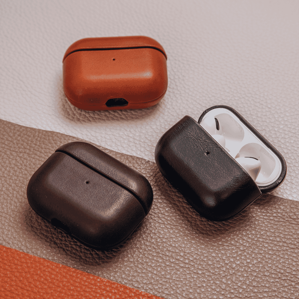 Three leather-cased earbud charging cases in black and shades of brown on a textured background.