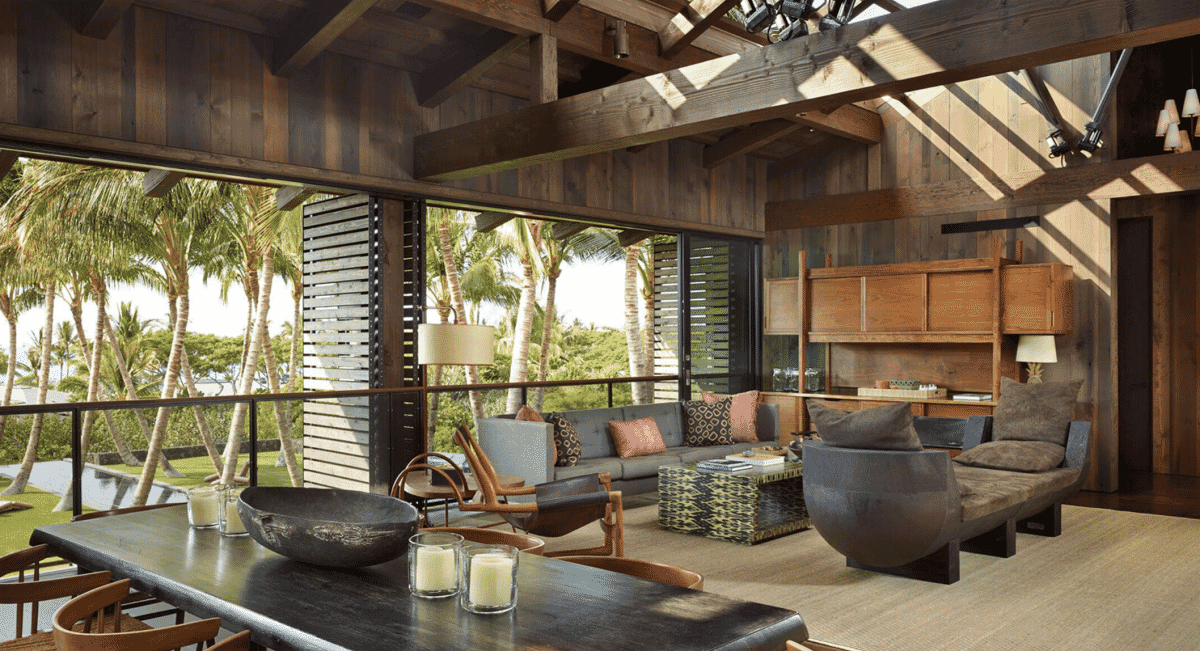 Interior view of a residence featuring large wood beams, modern furniture, and views of tropical greenery.