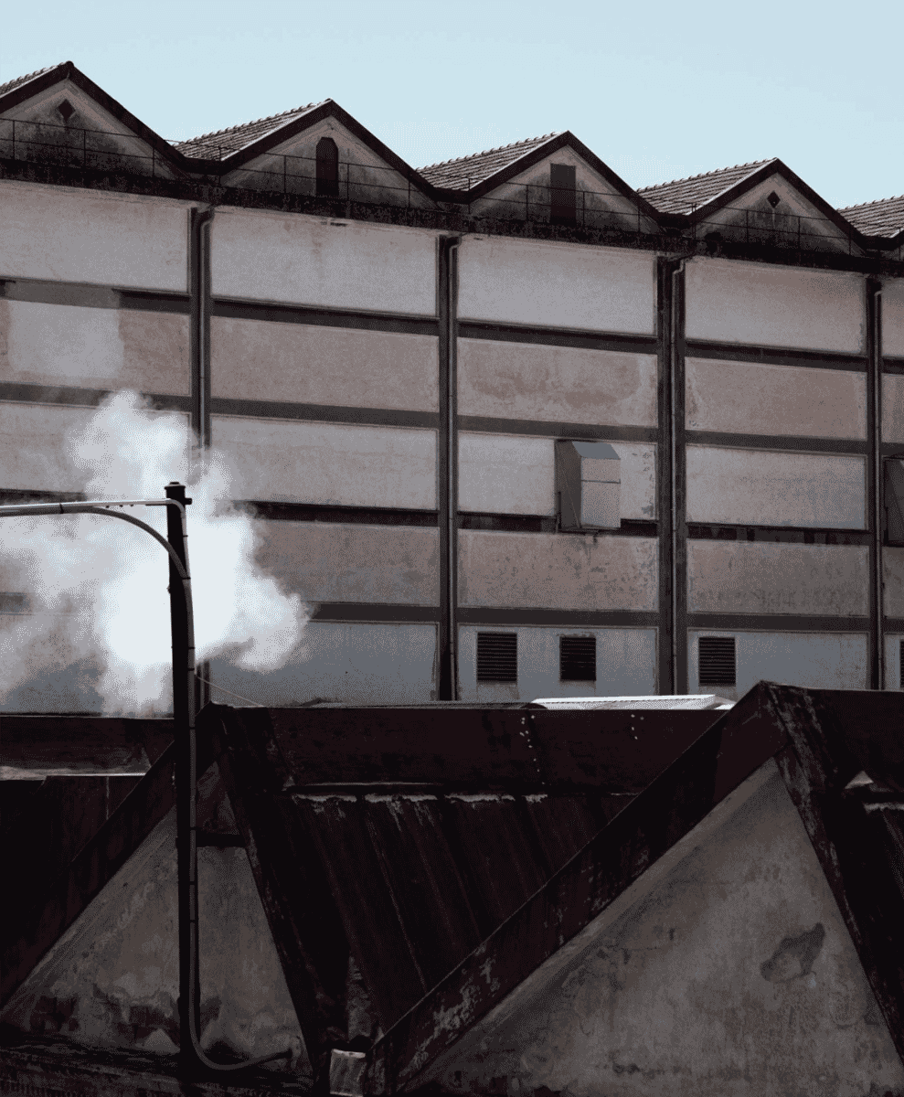 Industrial factory facade with weathered walls and steam vents under a clear sky.