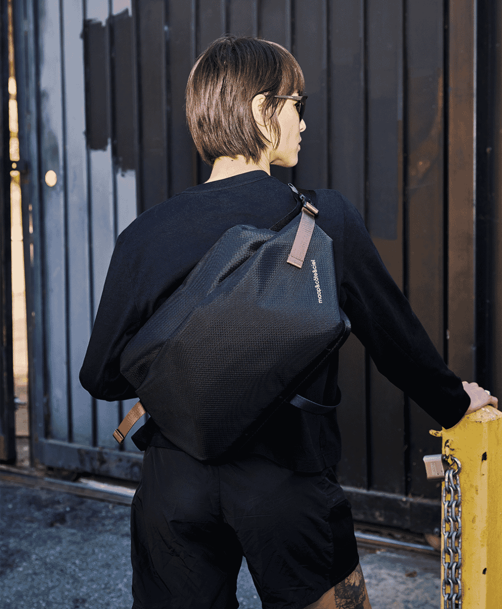 A person in black clothing wearing a black sling bag against a dark metal gate.