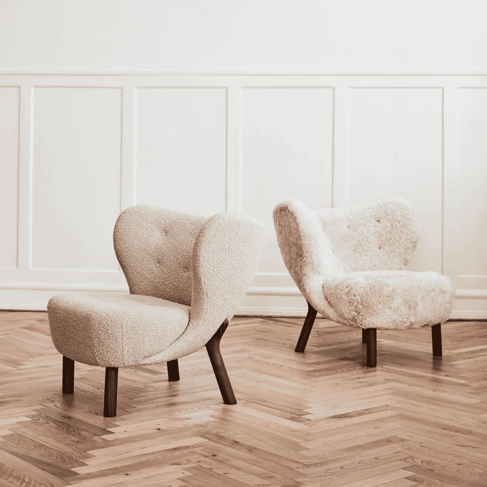 Two sheepskin-upholstered armchairs with dark wooden legs on hardwood flooring.
