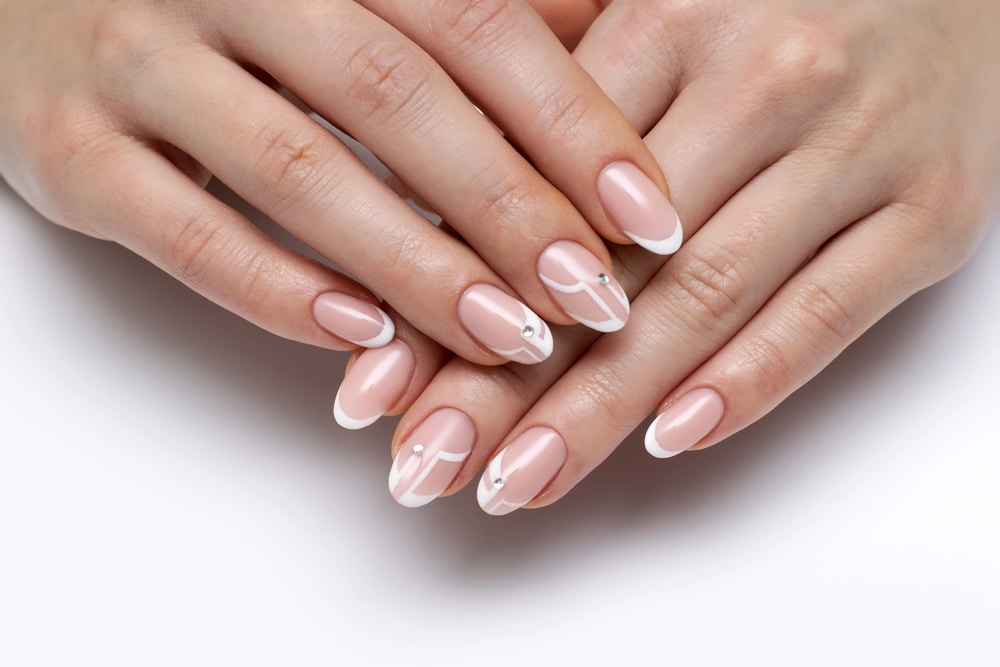 Elegantly manicured hands with pink and white French tips and small rhinestone accents.