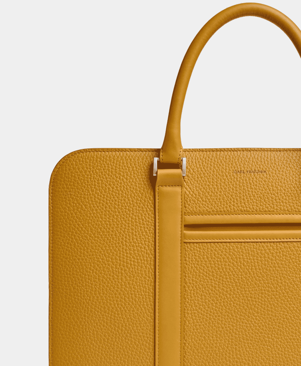 Close-up of a mustard-yellow pebbled leather briefcase featuring minimalist hardware.