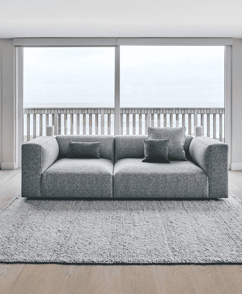 A gray textured sofa on a chunky knit rug in front of large windows with an ocean view.