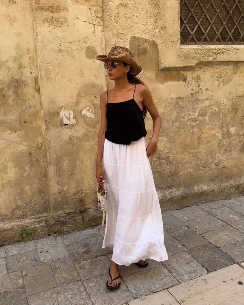 White tiered maxi skirt paired with a black spaghetti strap top and straw hat.