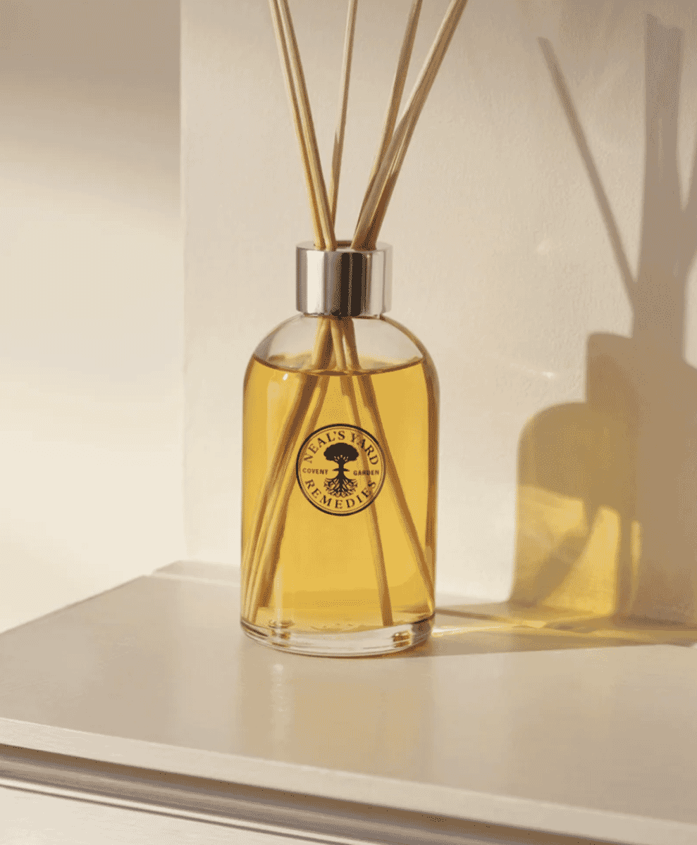 Close-up of a Neal's Yard Remedies reed diffuser in a sunlit, minimalist setting.