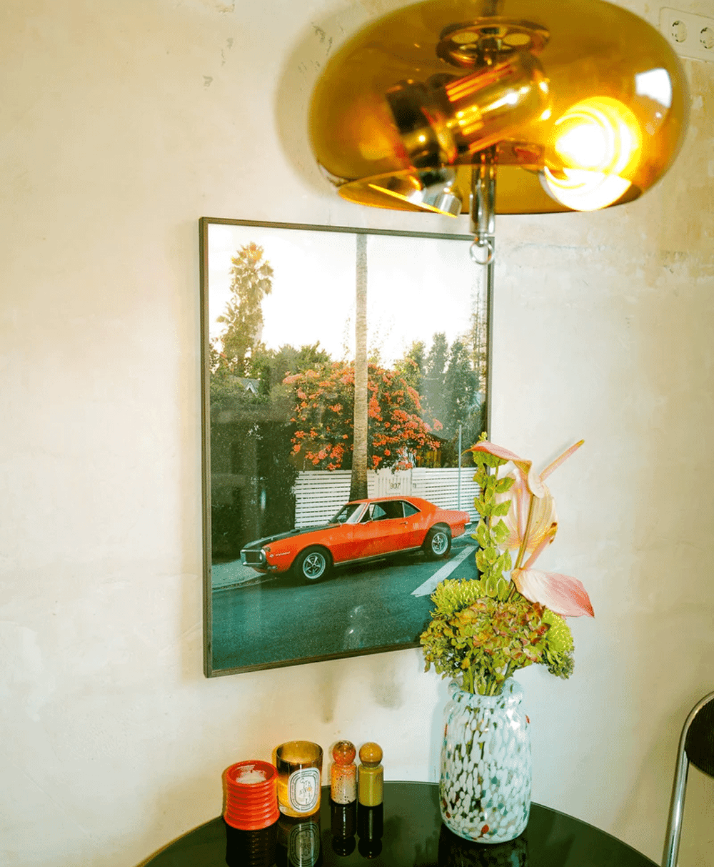 An orange muscle car art print hanging in a stylish interior with a gold lamp.