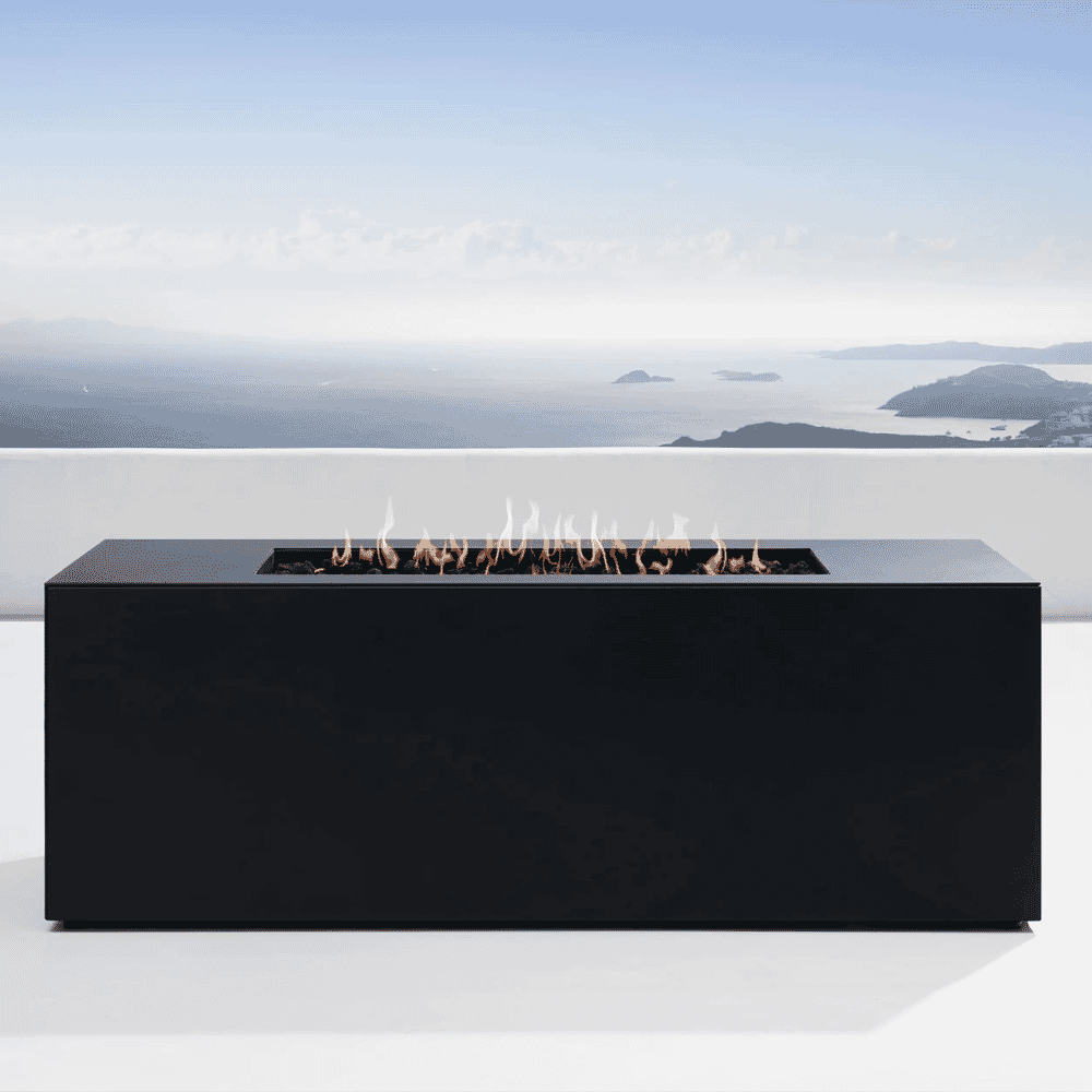 A minimalist black rectangular gas fire pit burning on a terrace overlooking the sea.