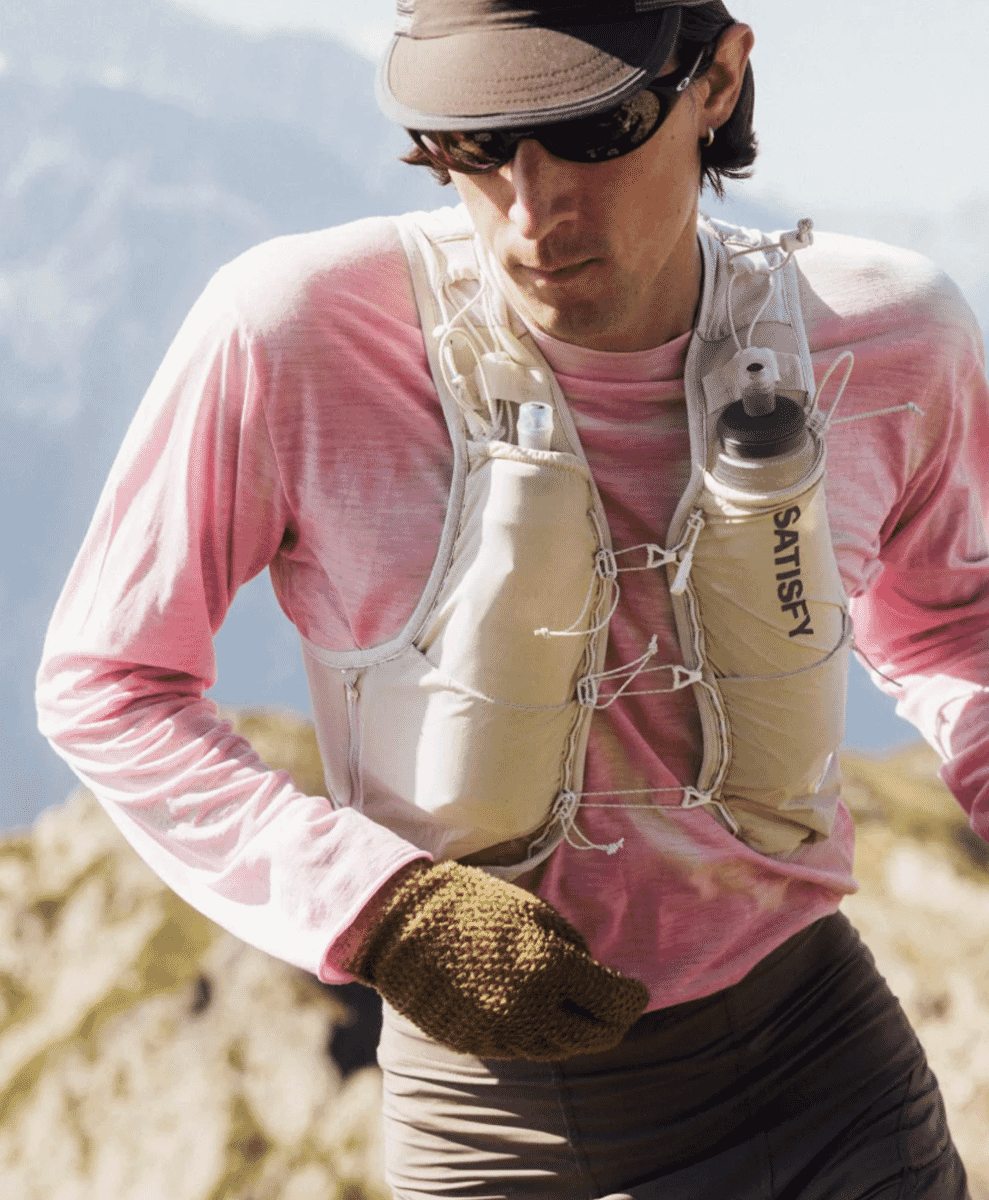 A trail runner navigating a rocky mountain path wearing a pink performance top and a beige hydration vest.