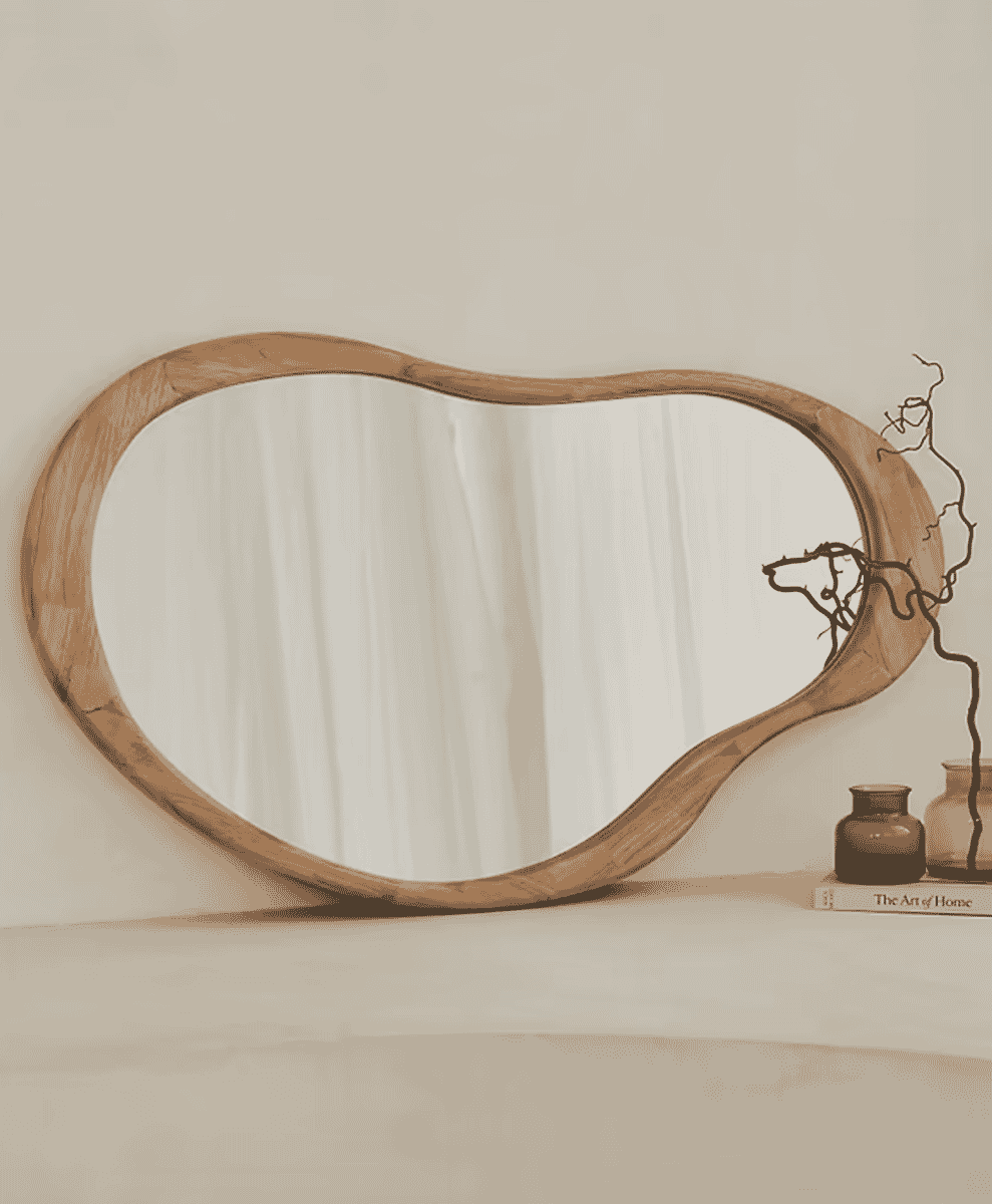 Irregularly shaped wooden-framed mirror on a neutral surface with minimalist decor.